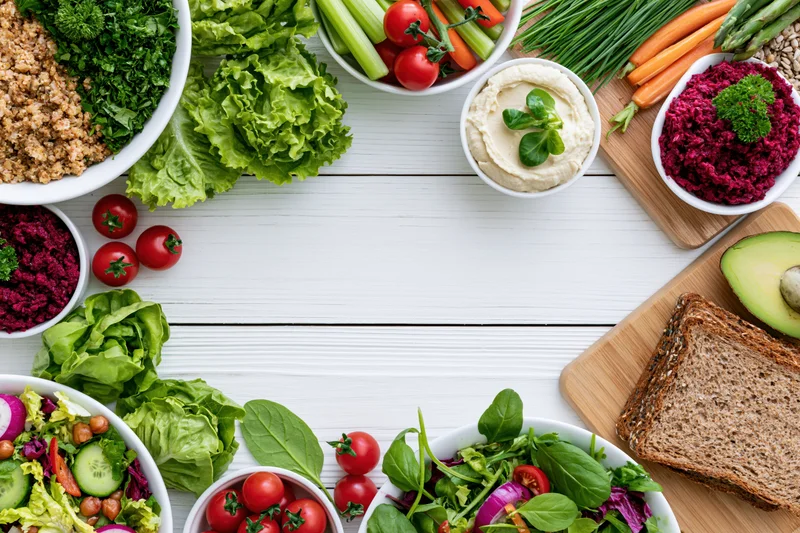 Overhead flat lay of assorted healthy vegetarian dishes and ingredients arranged on white wooden table with copyspace