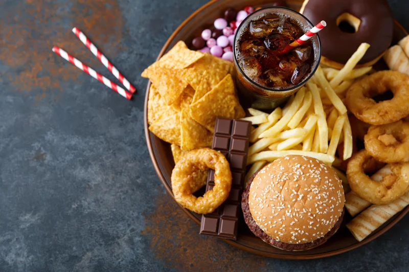 Overhead flat lay of assorted junk food on a dark surface with copyspace