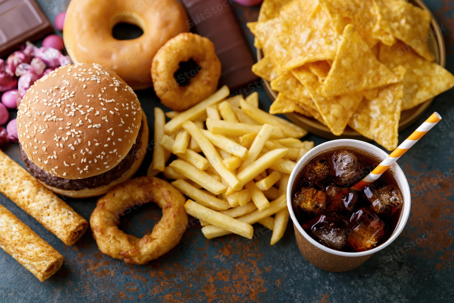 Overhead flat lay of assorted junk food spread across a dark surface