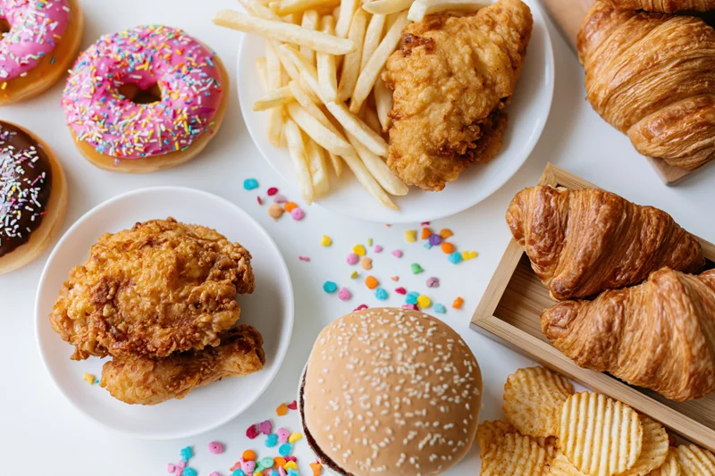 Assorted junk food arranged in a flat lay on a white surface with plates and a wooden tray