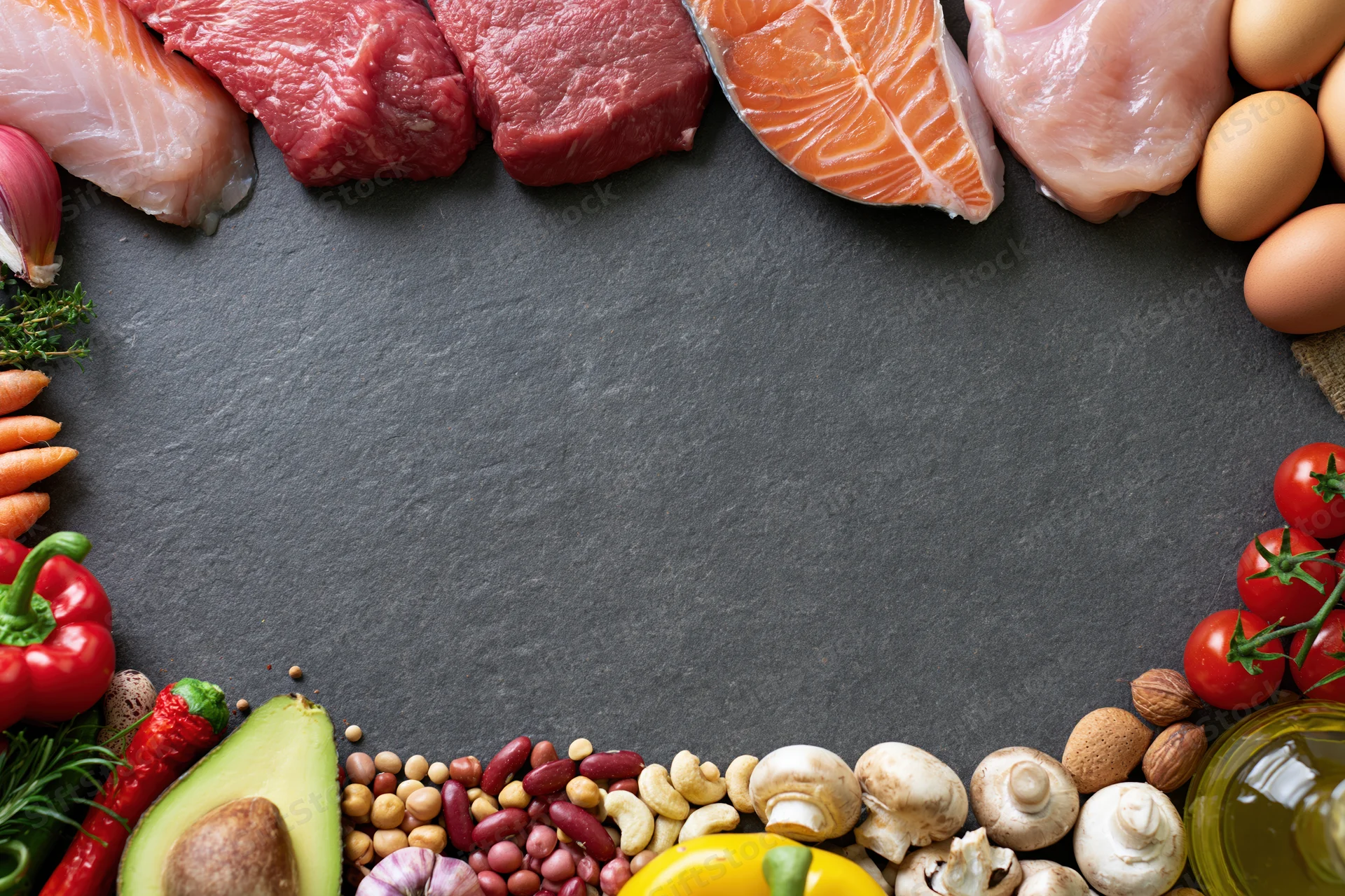 Assorted whole foods arranged in a border around a dark surface with copyspace in center