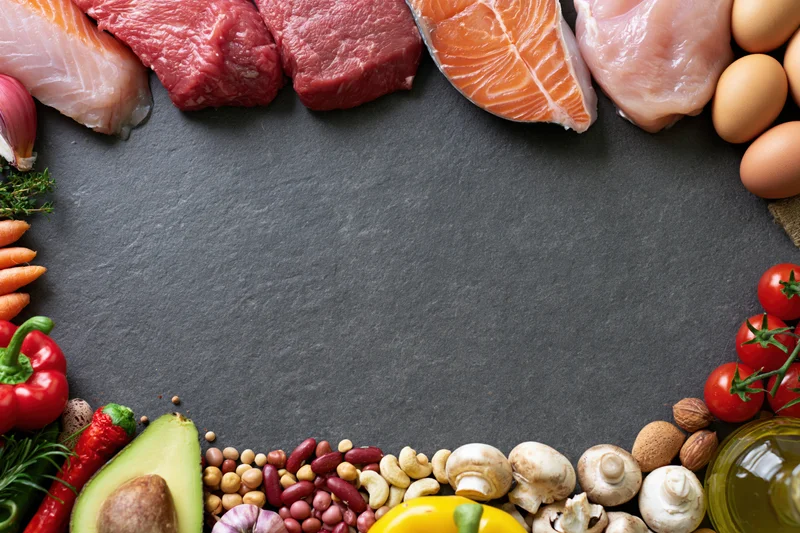 Assorted whole foods arranged in a border around a dark surface with copyspace in center