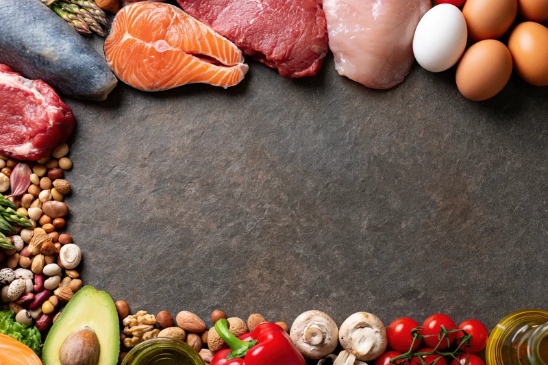 Assorted whole foods arranged in a border around a dark surface with copyspace in center