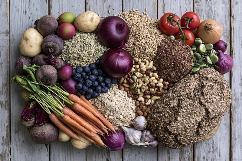 Overhead flat lay of assorted whole foods densely arranged on wooden surface