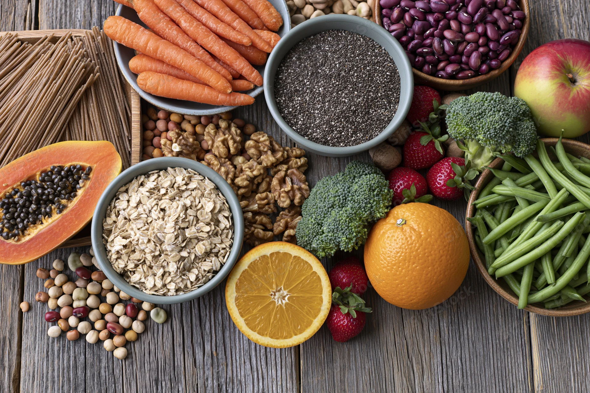Overhead flat lay of assorted whole foods including fruits vegetables grains and seeds on wooden surface
