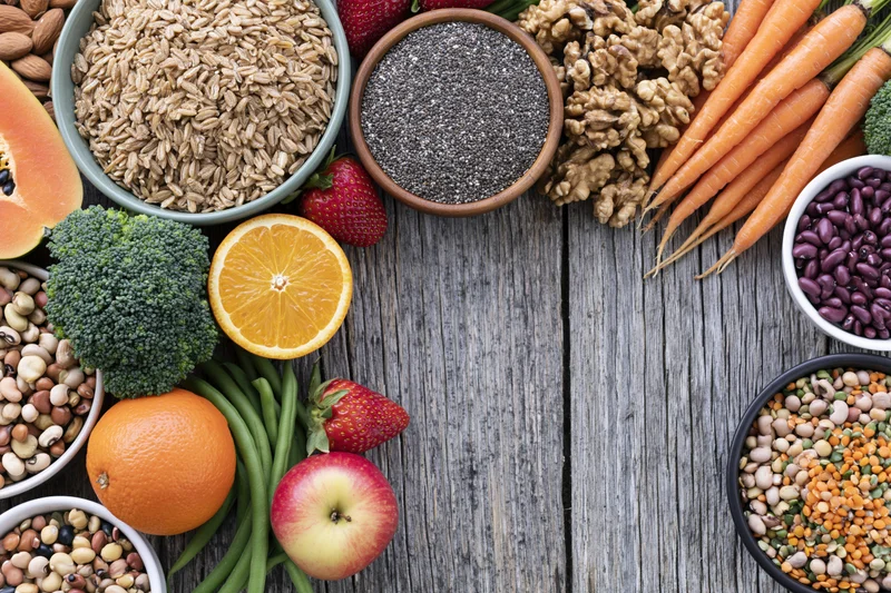 Overhead flat lay of assorted whole foods including fruits vegetables grains seeds nuts and beans on wooden surface with copyspace