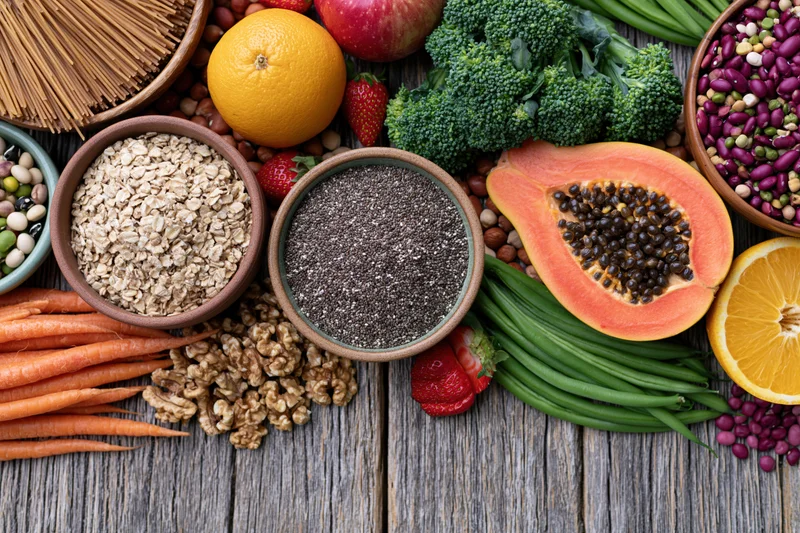 Overhead flat lay of assorted whole foods including fruits vegetables grains seeds and nuts on wooden surface