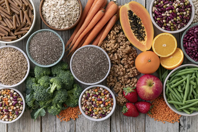 Overhead flat lay of assorted whole foods including fruits vegetables grains legumes on wooden surface