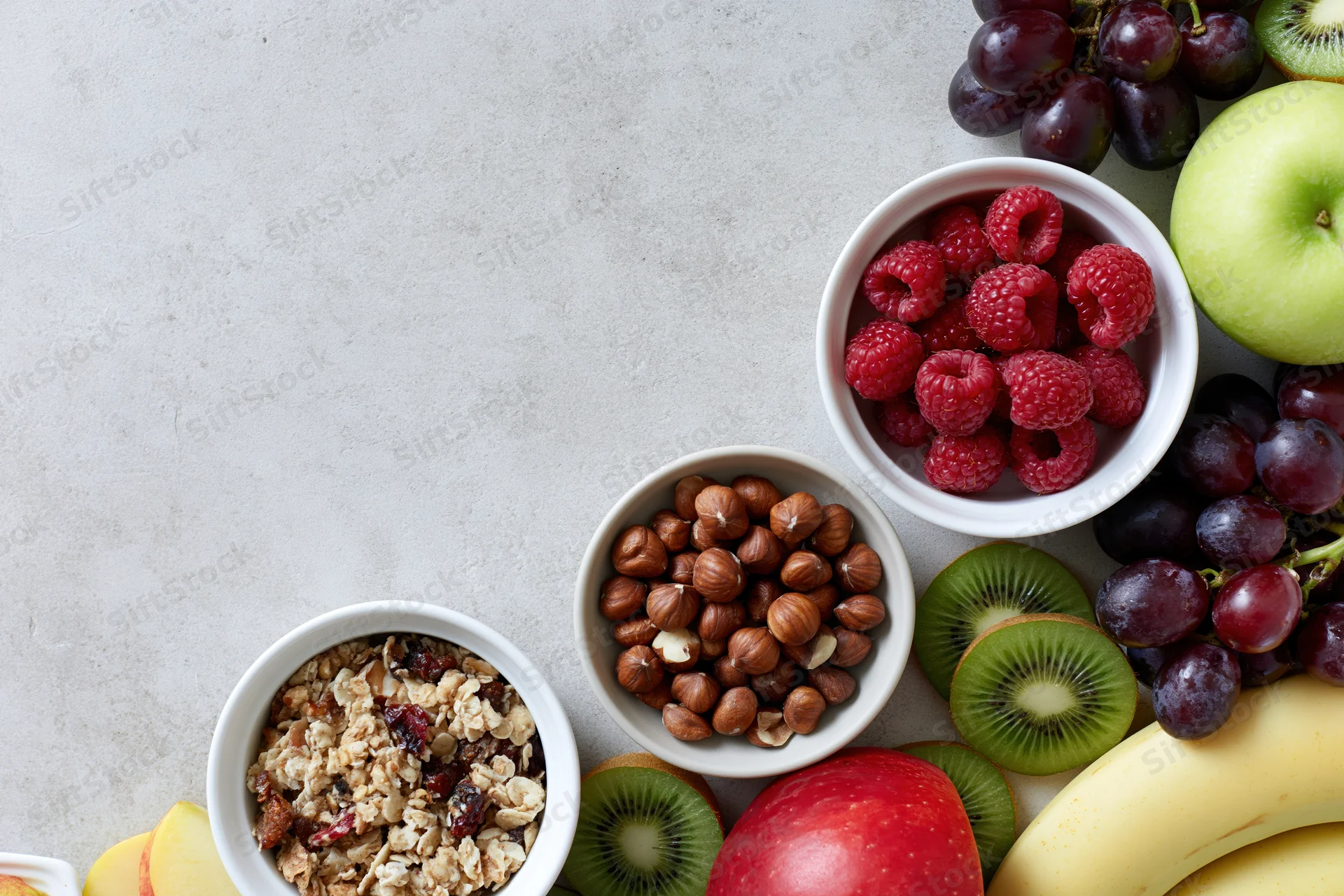 Breakfast ingredients arranged in bowls and clusters along the right side of a light surface with copyspace on the left