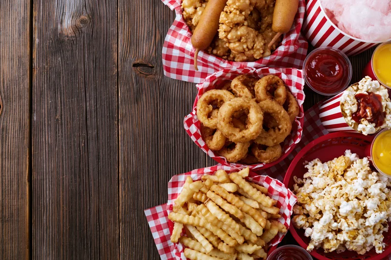 Overhead flat lay of classic american fair food spread on wooden table with red and white checkered baskets and condiments