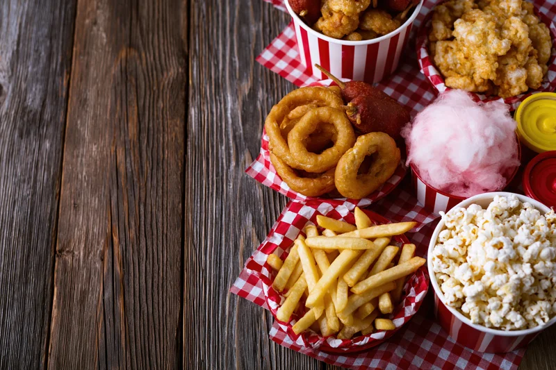 Classic american fair food spread arranged on a wooden table with red and white checkered paper baskets and striped buckets, overhead view