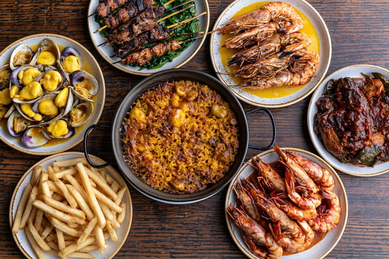 Overhead flat lay of eight spanish tapas and seafood dishes arranged on a wooden table
