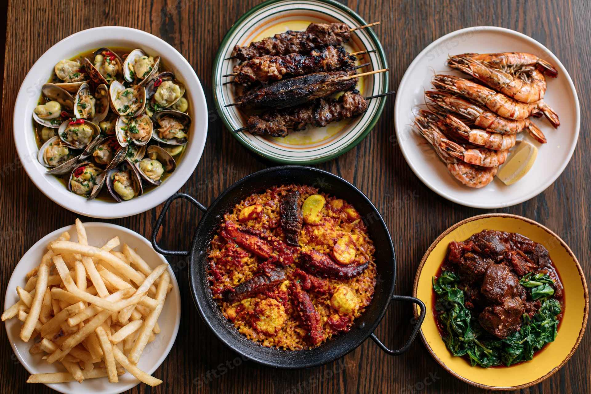 Overhead flat lay of spanish tapas and seafood dishes on wooden table