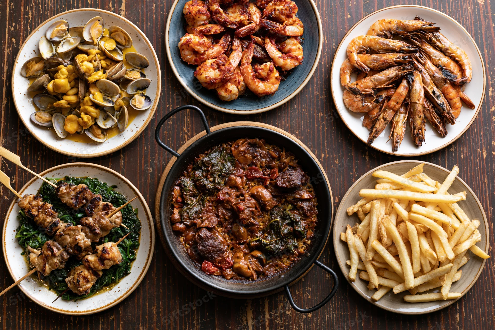Overhead flat lay of spanish tapas and seafood dishes arranged on a wooden table