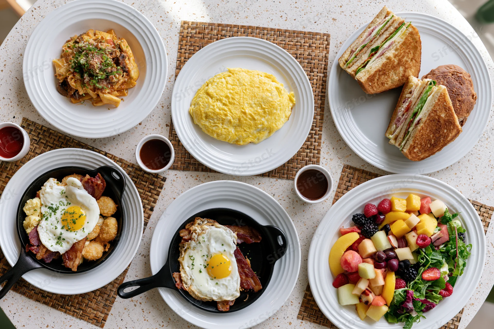 Overhead flat lay of diverse brunch dishes arranged on a table with plates, skillets, and placemats