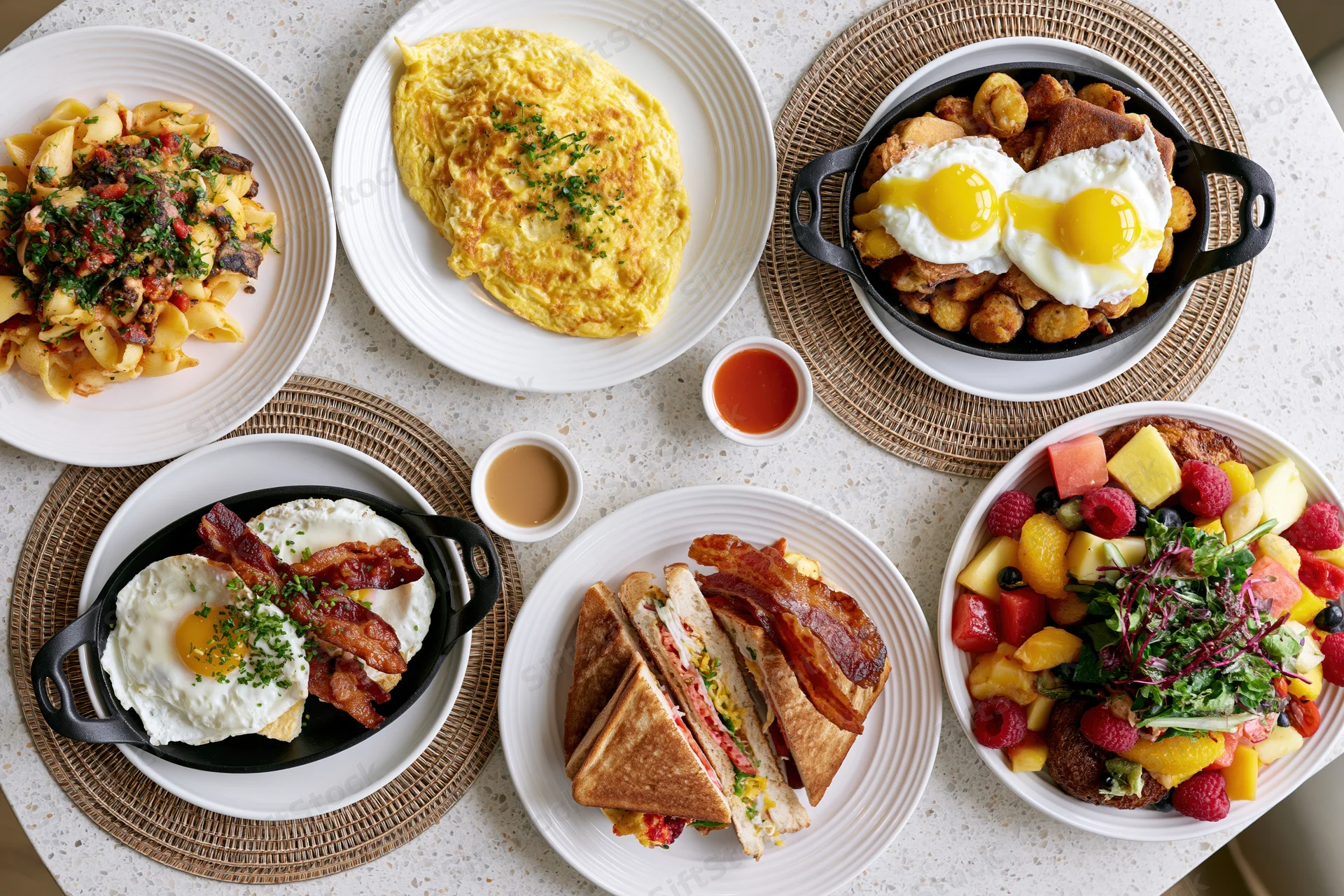 Overhead flat lay of diverse brunch dishes arranged on a table with plates, skillets, and placemats
