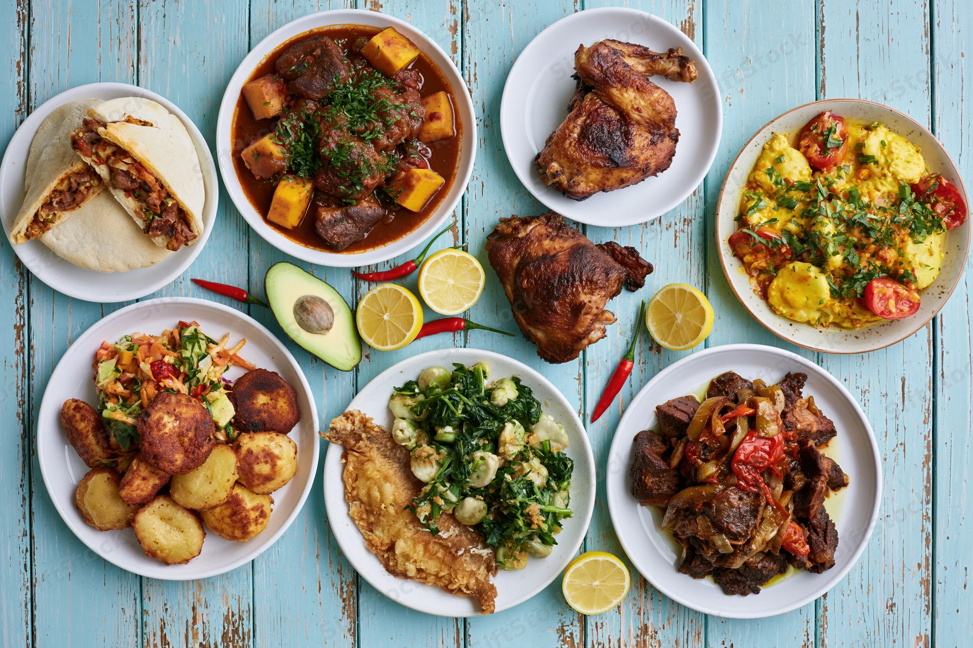 Overhead flat lay of eight varied dishes arranged on a blue wooden table