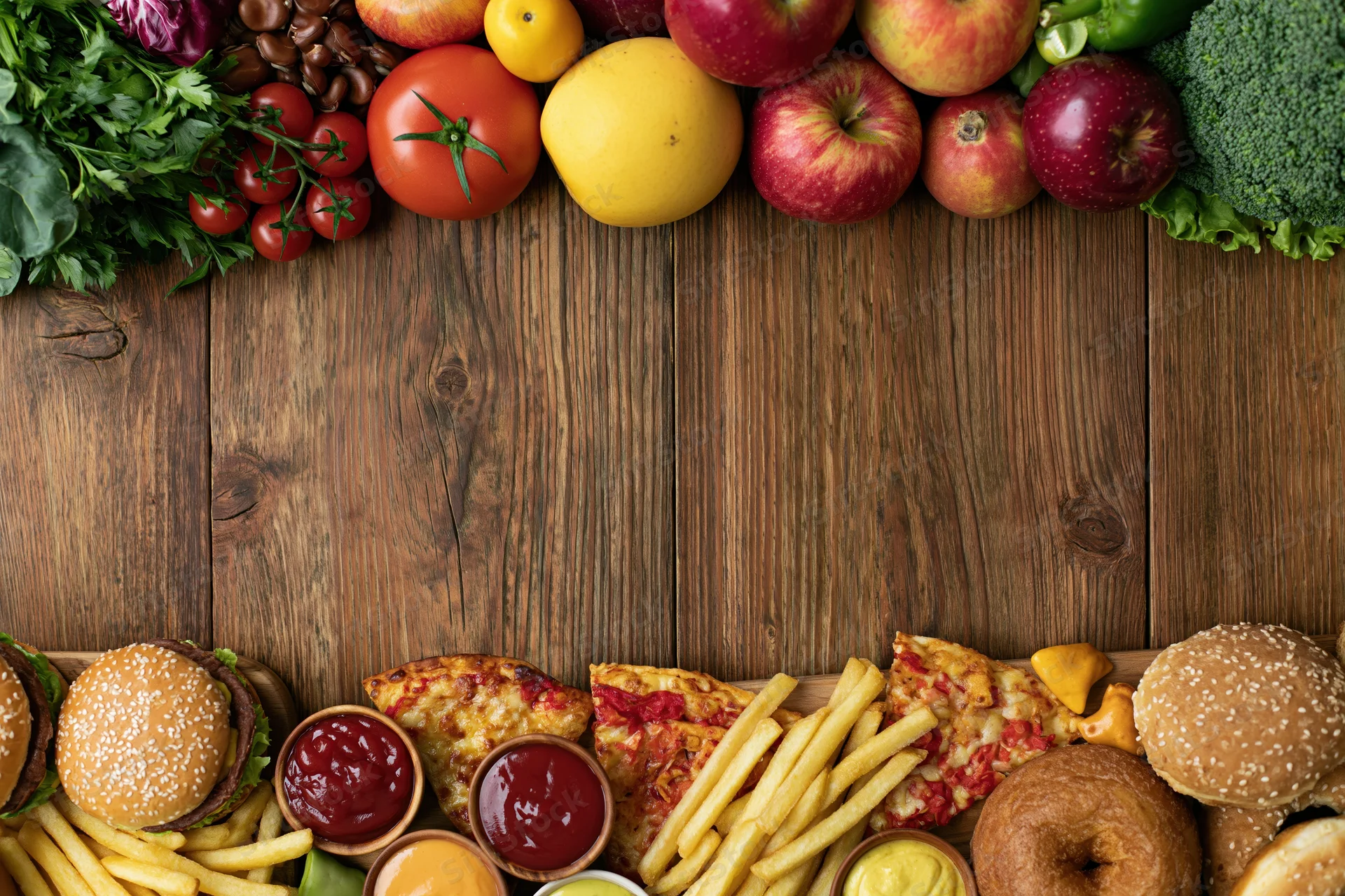 Fresh fruits and vegetables arranged at top of wooden table with fast food items at bottom