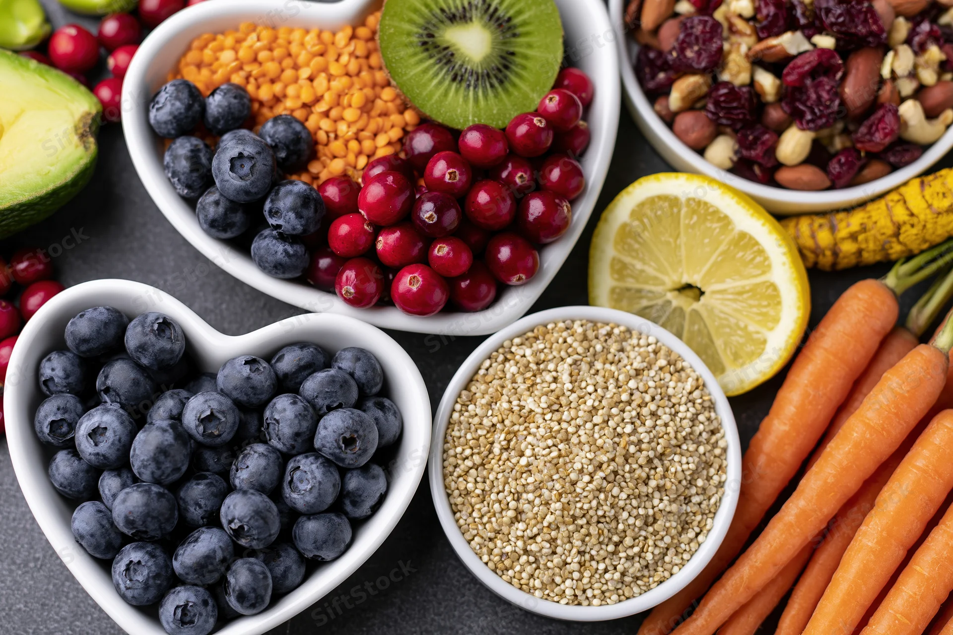 Overhead flat lay of fresh fruits vegetables grains and nuts arranged in white bowls on dark surface
