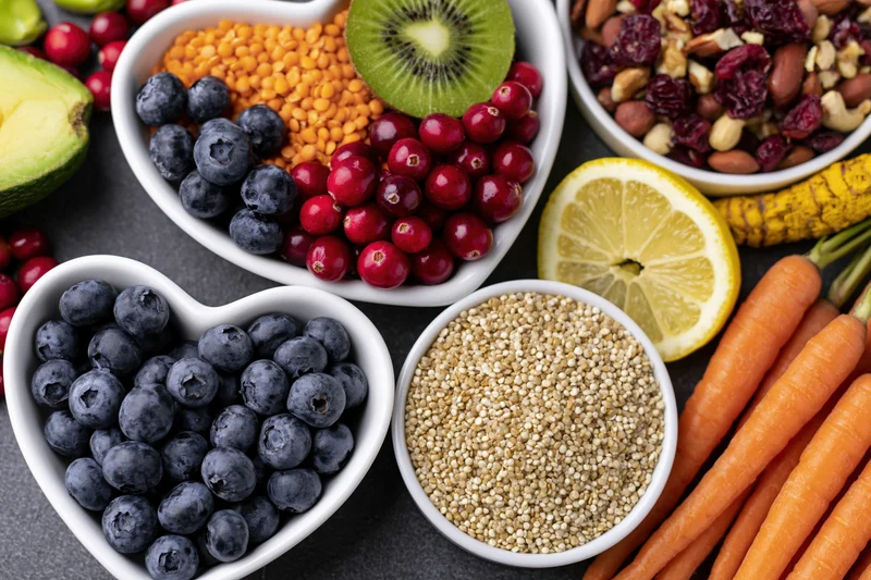 Overhead flat lay of fresh fruits vegetables grains and nuts arranged in white bowls on dark surface