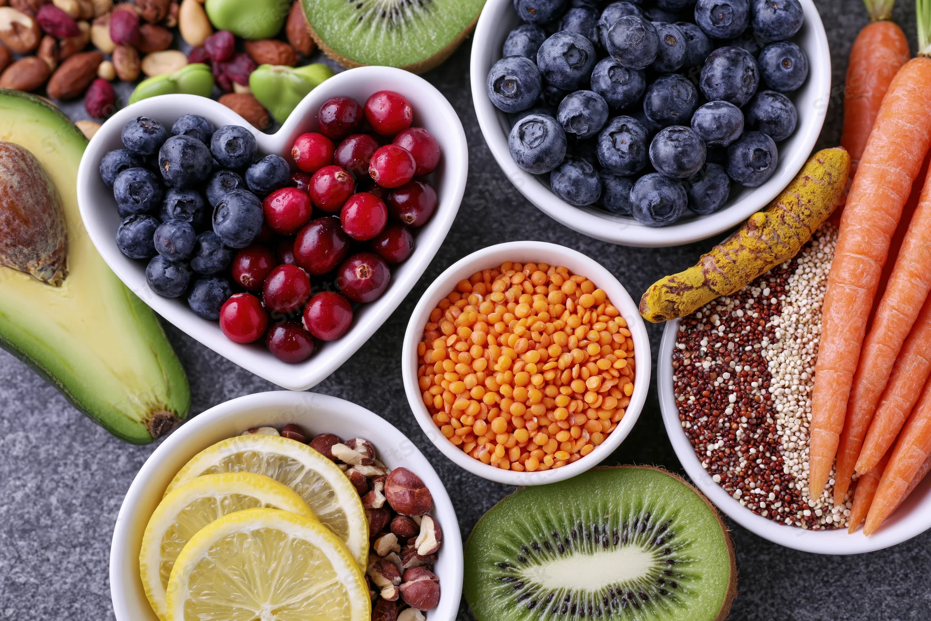 Overhead flat lay of fresh fruits vegetables grains and nuts arranged on dark surface