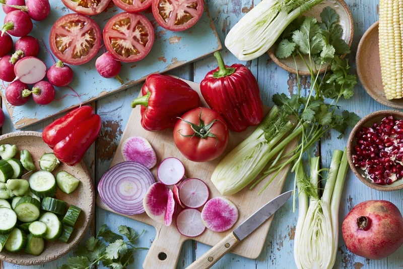 Fresh vegetables and fruits arranged on a wooden cutting board and rustic surface for meal preparation