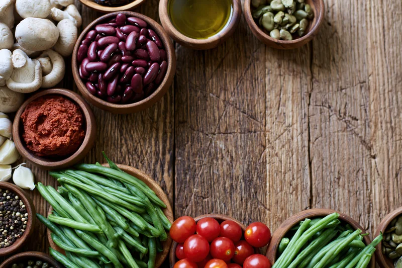 Overhead flat lay of fresh vegetables and pantry ingredients arranged in wooden bowls on a rustic wooden table
