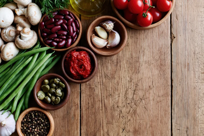 Fresh vegetables and pantry ingredients arranged on a wooden table in overhead flat lay