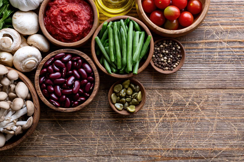 Overhead flat lay of fresh vegetables and pantry ingredients arranged on a wooden table