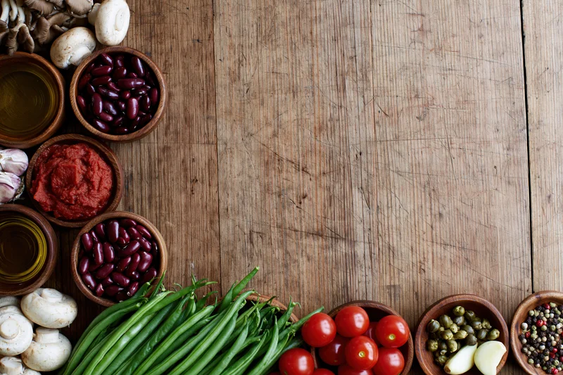Fresh vegetables and pantry ingredients arranged in wooden bowls on a rustic wooden surface in overhead flat lay with copyspace