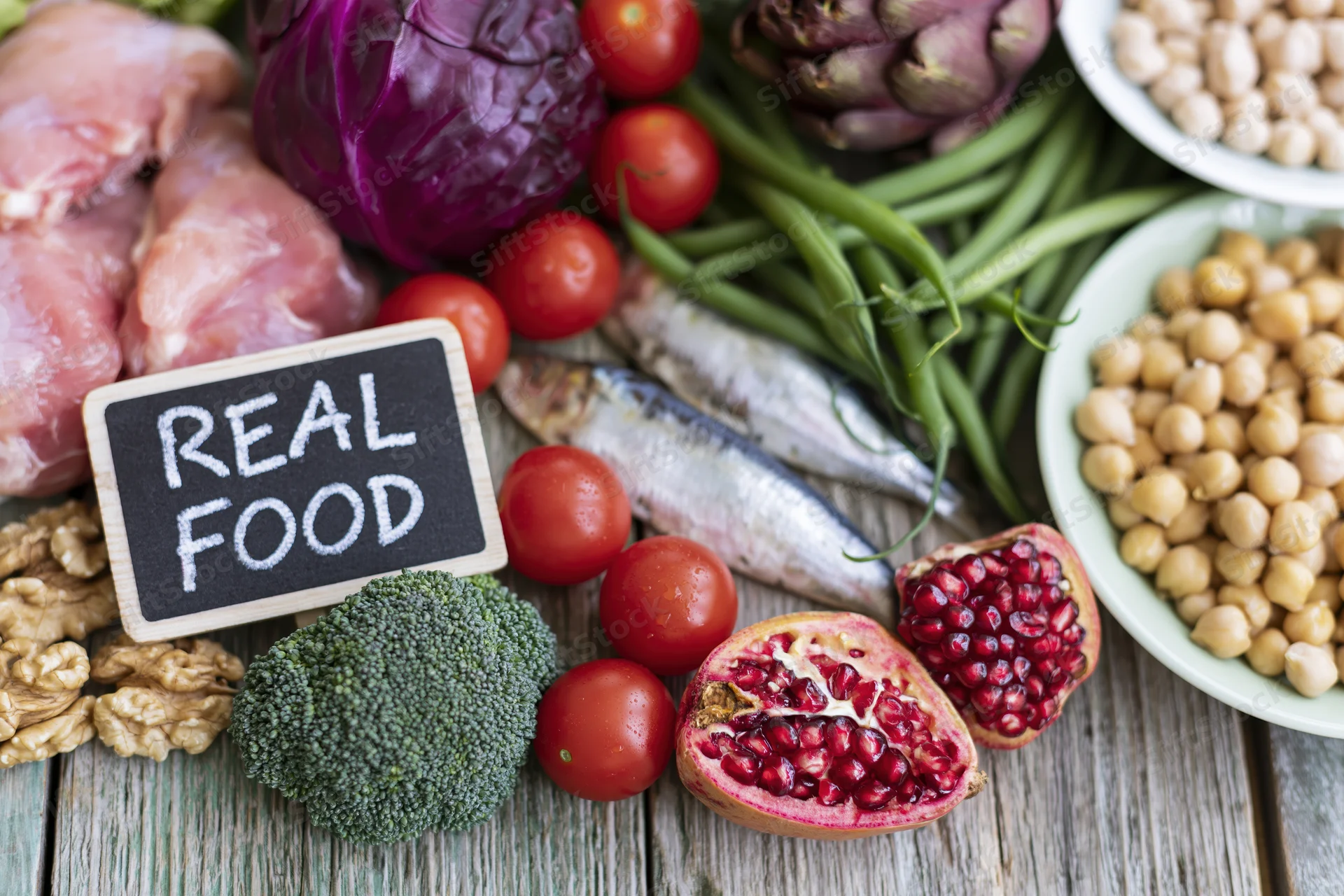 Fresh whole foods arranged around a chalkboard sign reading real food on a wooden table