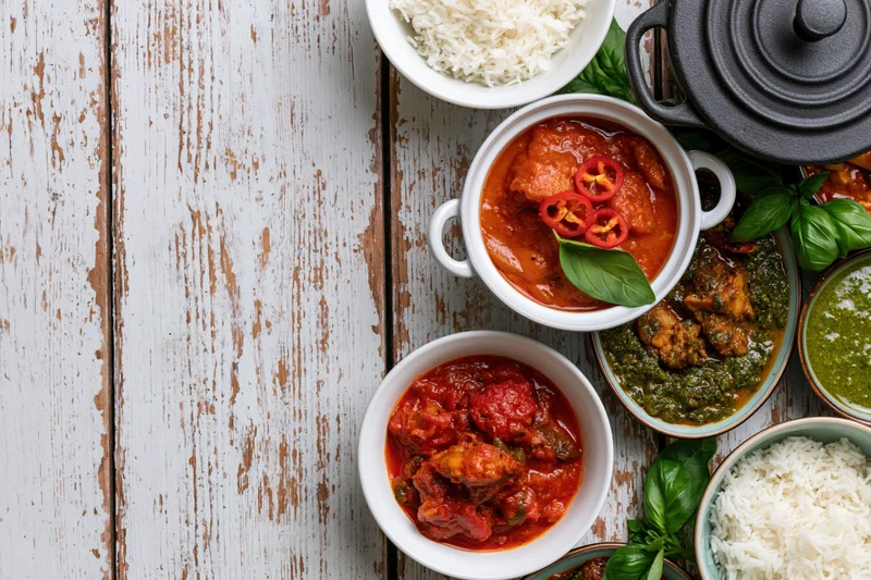Multiple curry dishes and rice bowls arranged on a rustic white wooden table in overhead flat lay view