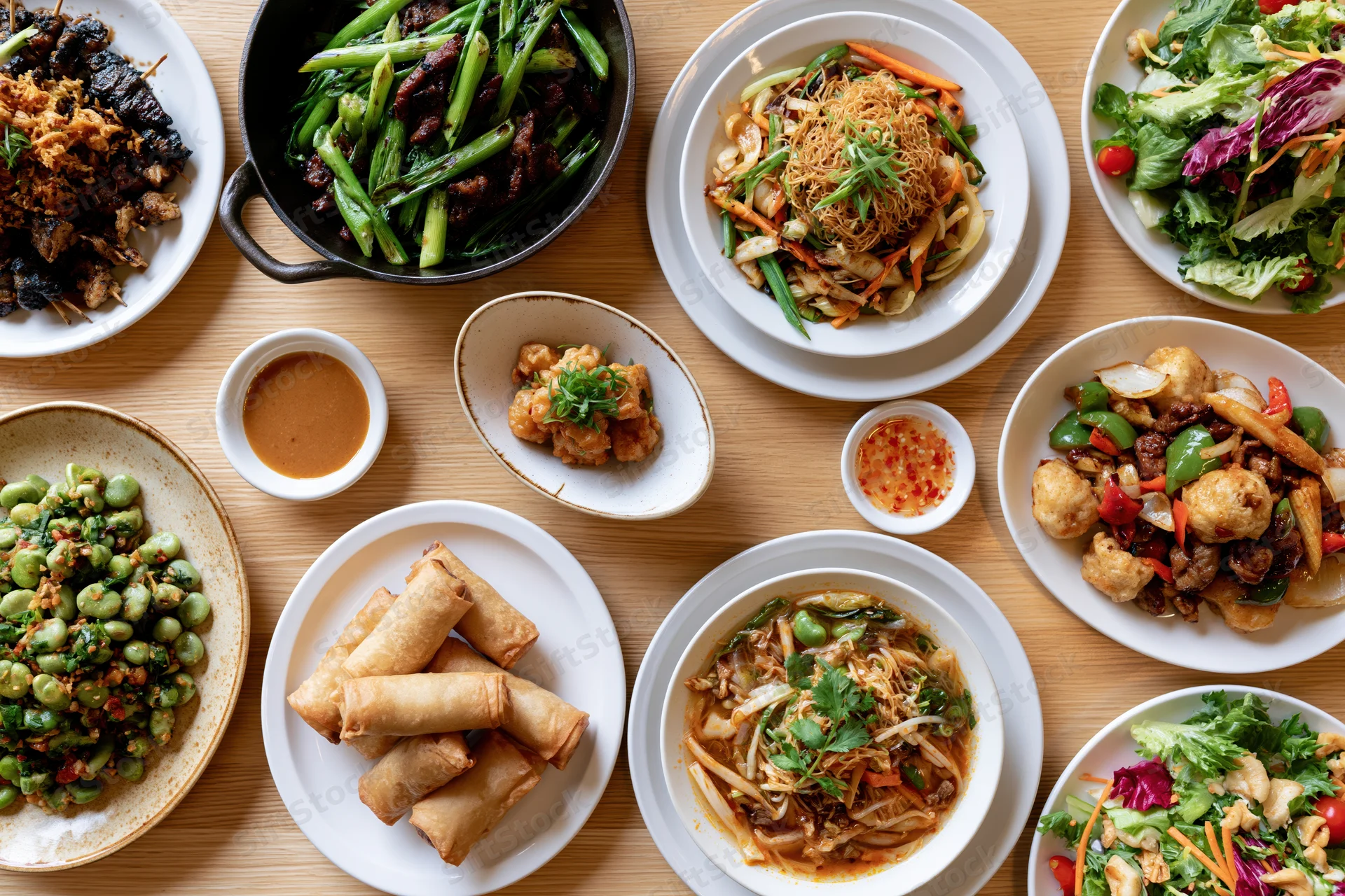 Overhead view of multiple Asian and Western dishes arranged on a wooden table