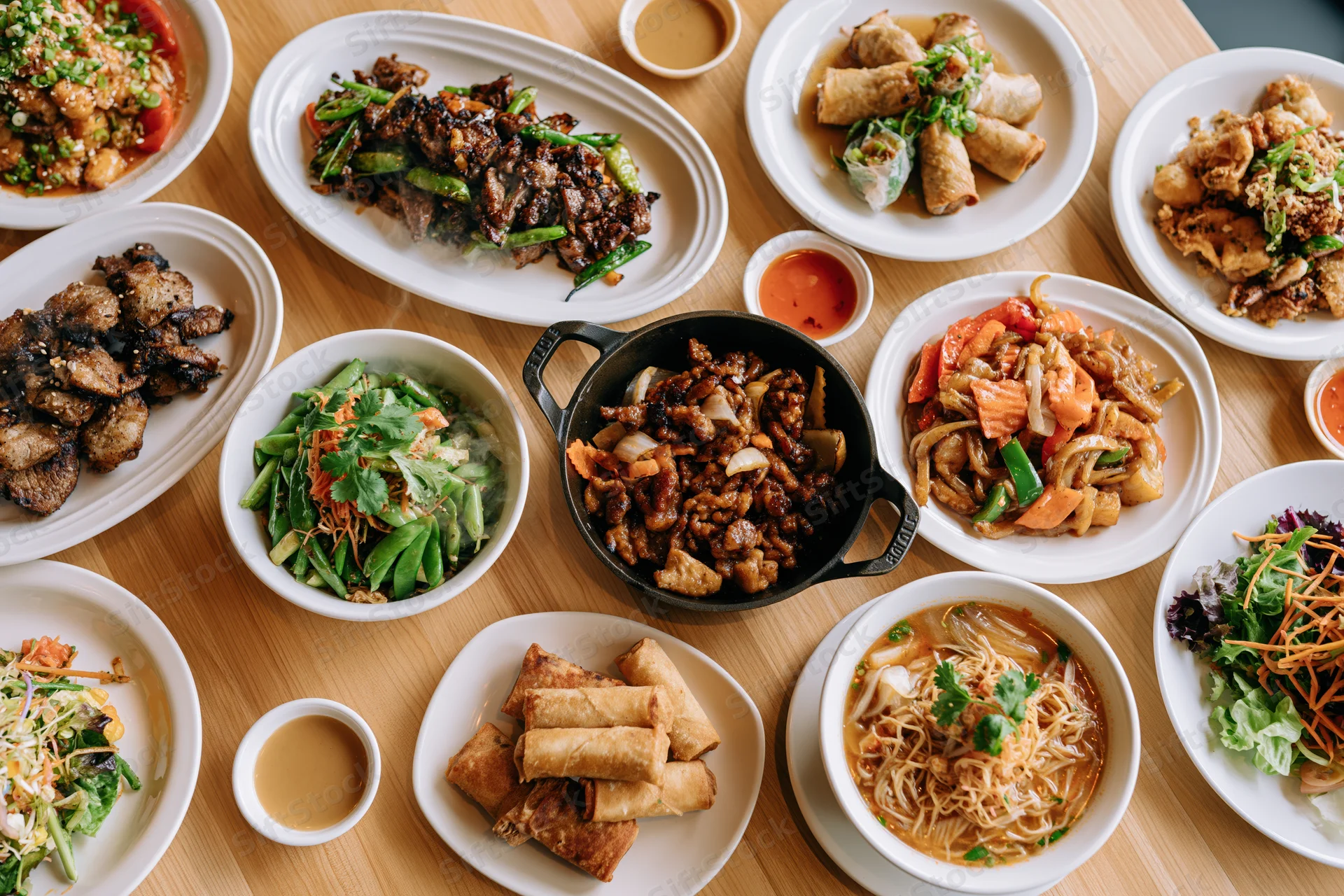 Overhead view of multiple Asian and Western dishes arranged on a wooden table for a shared meal