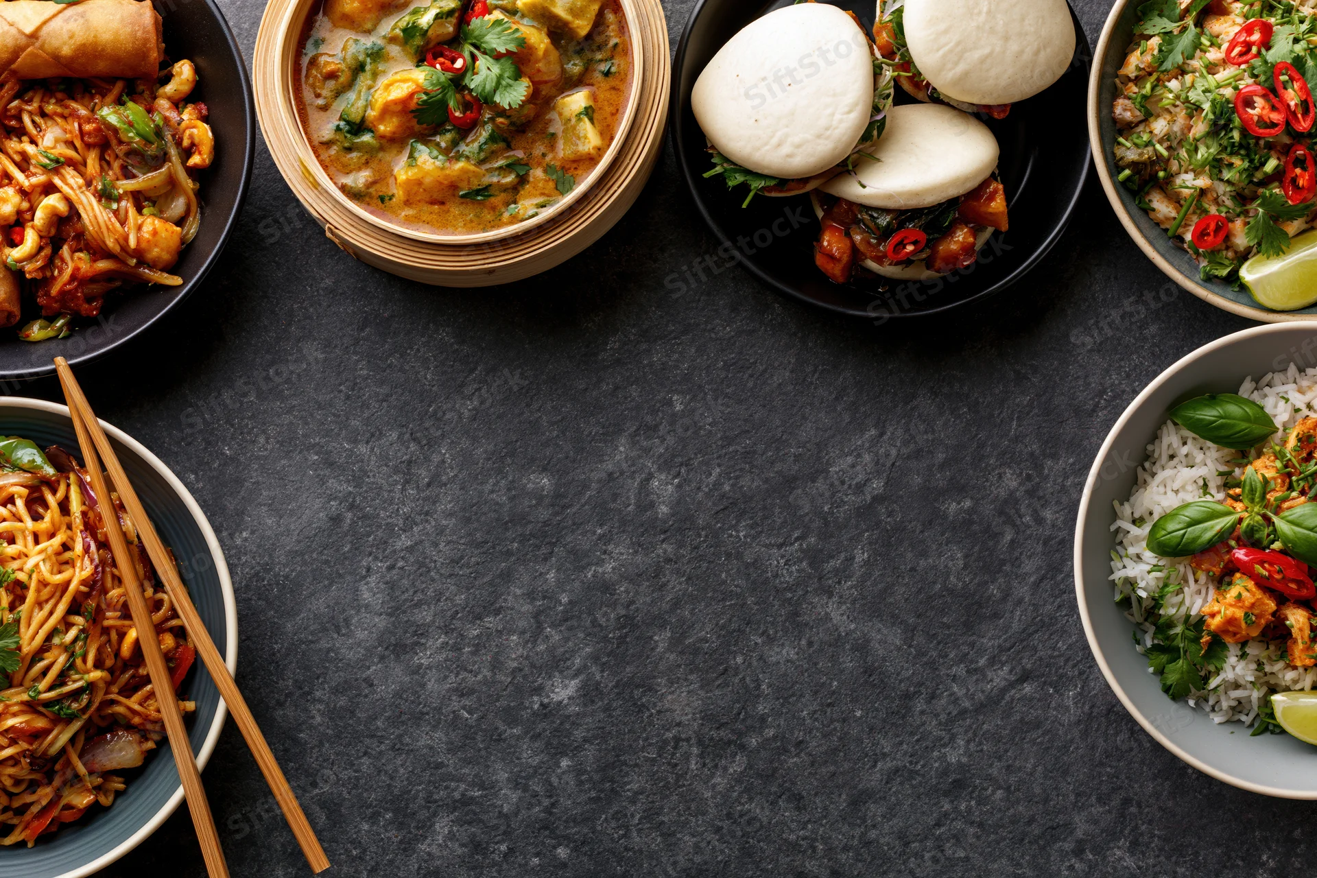Multiple asian dishes arranged in a flat lay on a dark textured surface with copyspace in center