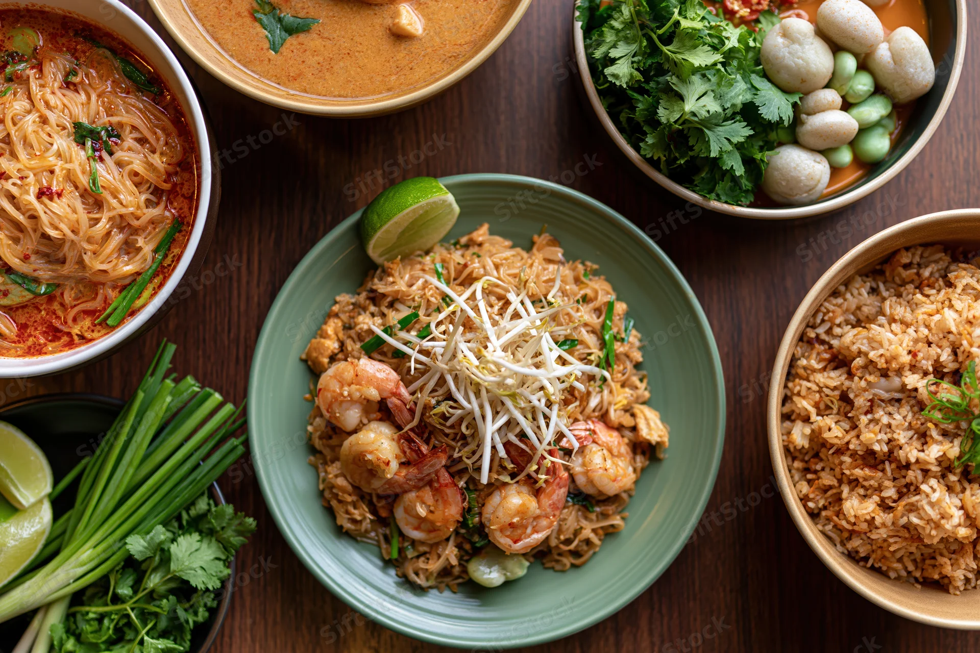 Overhead flat lay of multiple thai dishes arranged on a dark wooden table