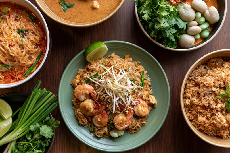 Overhead flat lay of multiple thai dishes arranged on a dark wooden table