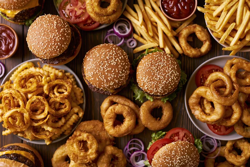 Overhead flat lay of multiple burgers and large portions of french fries and onion rings on a wooden table