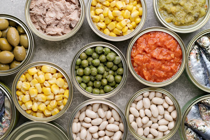 Overhead flat lay of open tin cans filled with various canned foods arranged on a gray surface