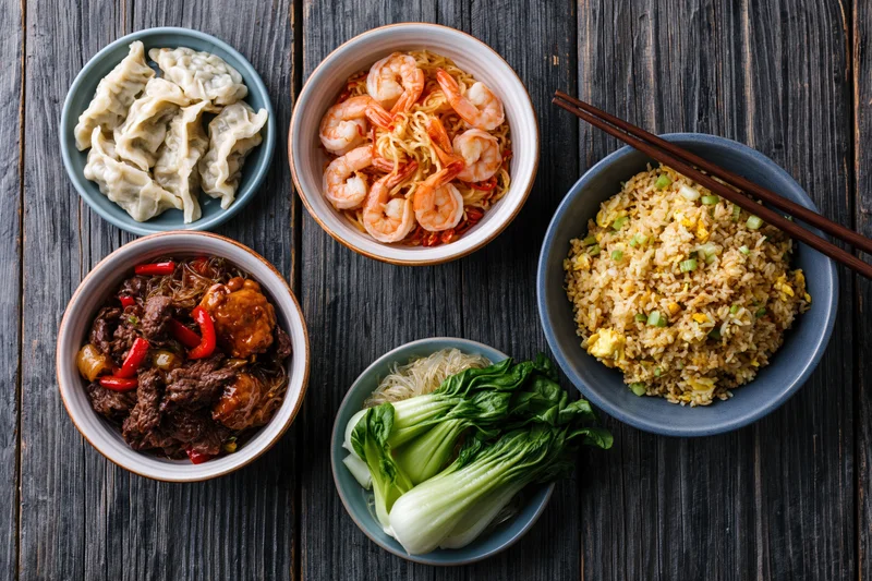 Overhead flat lay of five asian dishes arranged in a circle on dark wooden table