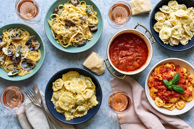 Six pasta dishes arranged overhead on a table with wine and utensils