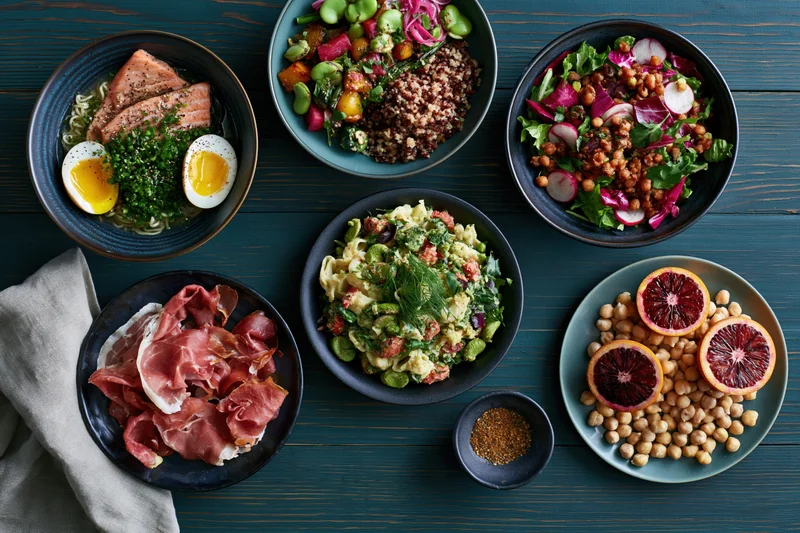 Six meal bowls and plates arranged overhead on a dark blue wooden table