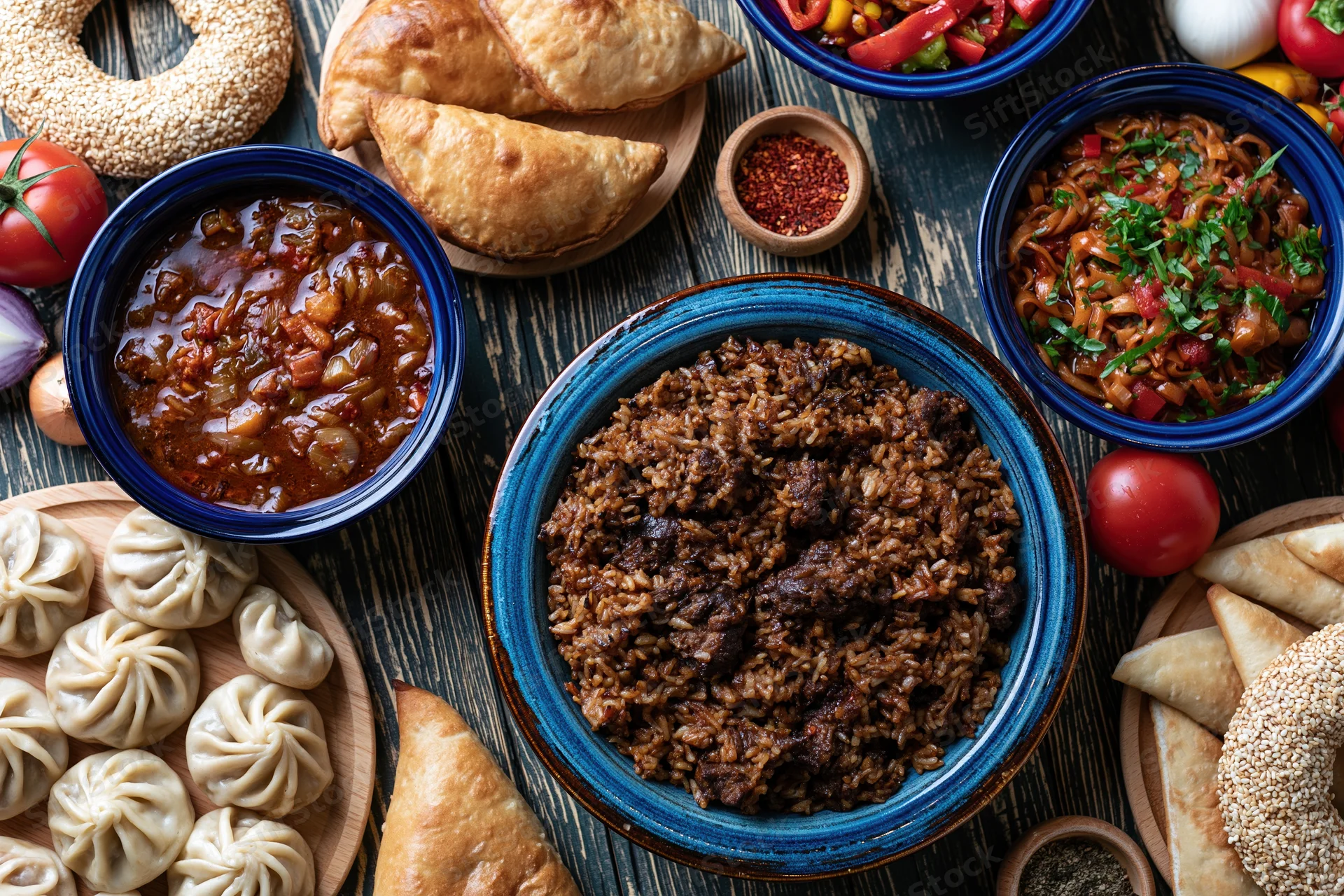 Overhead flat lay of central asian plov with meat and rice served with dumplings, samosas, and vegetables on a wooden table