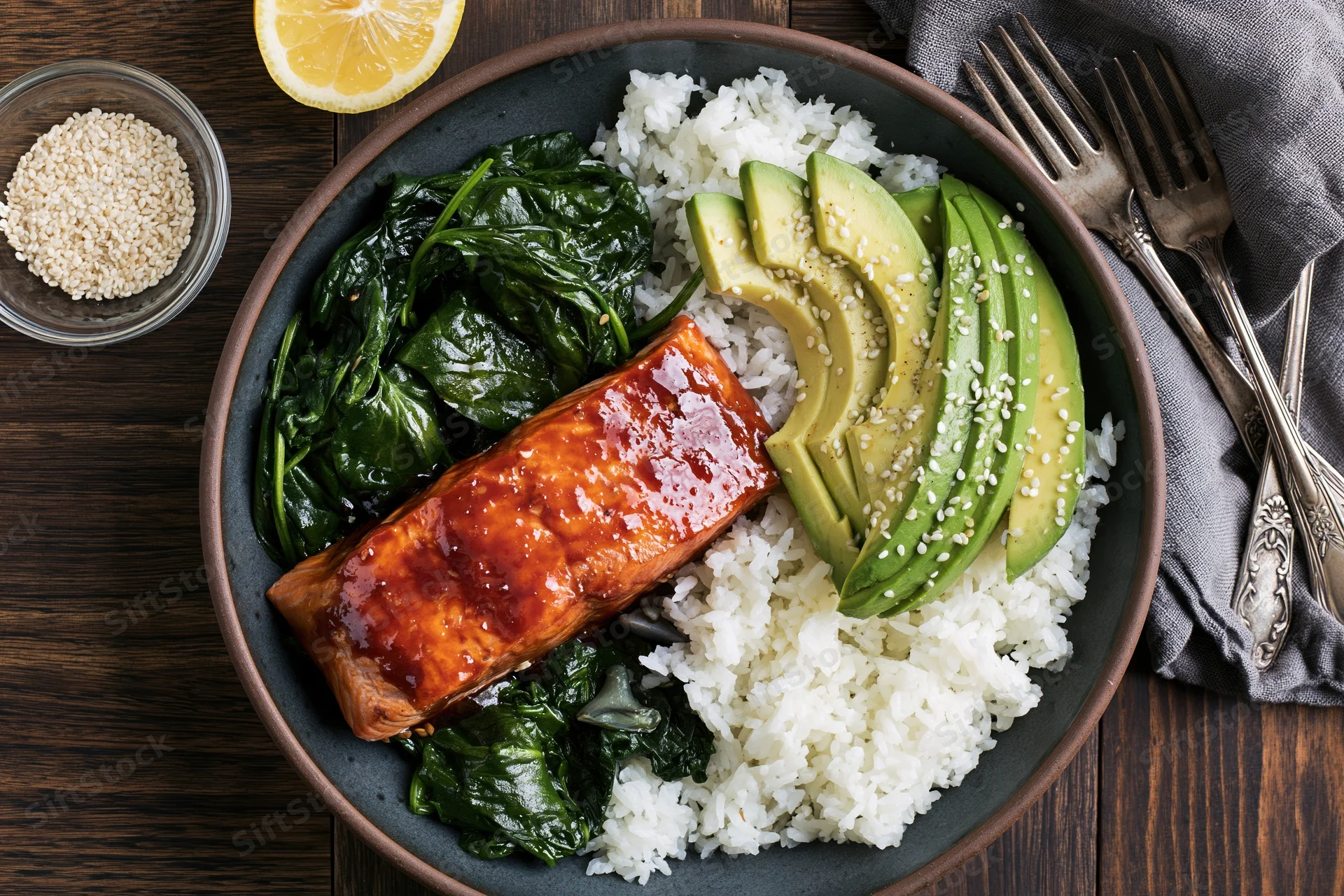 Glazed salmon with rice, avocado, and spinach in a dark ceramic bowl on a wooden table