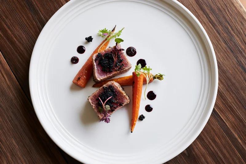 Two seared tuna medallions with carrots and garnish on a white plate on a wooden table
