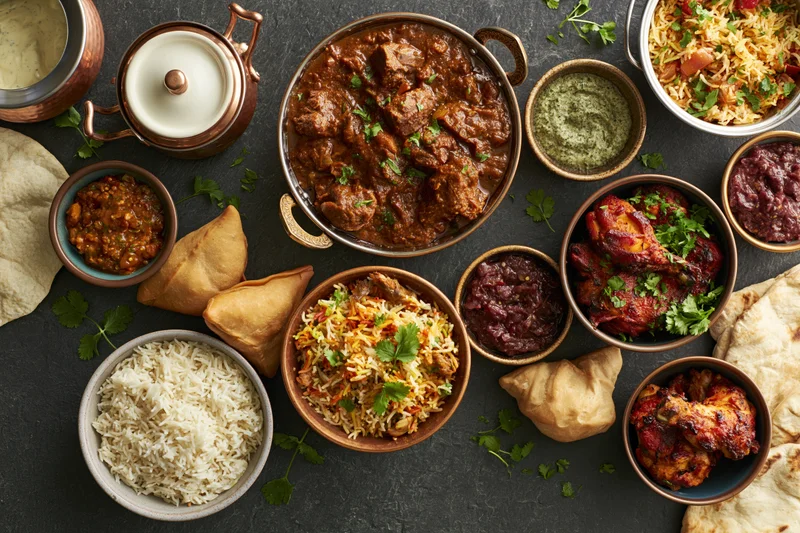 Overhead spread of indian dishes arranged on dark slate surface