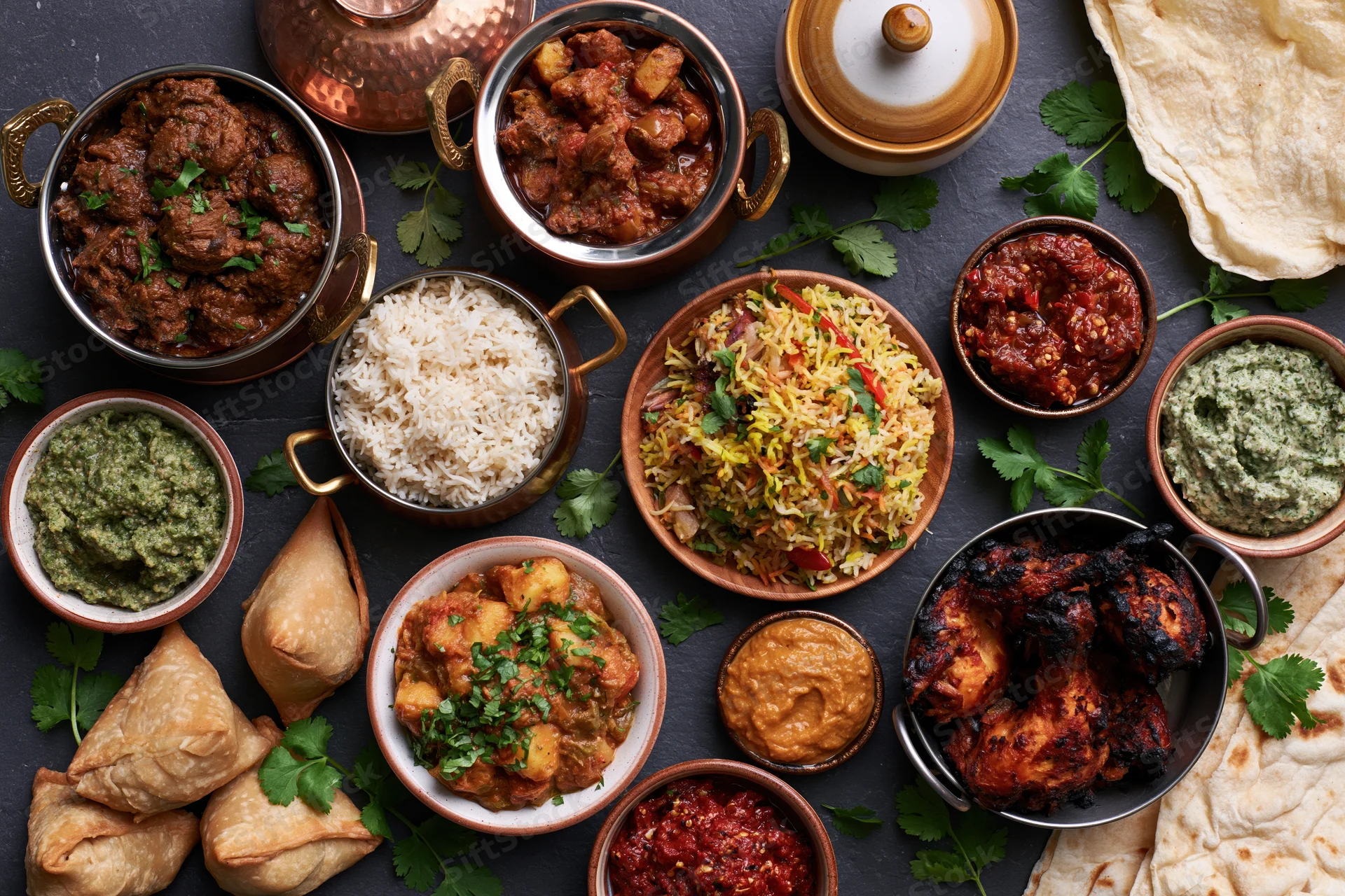 Overhead spread of indian dishes arranged on dark slate surface