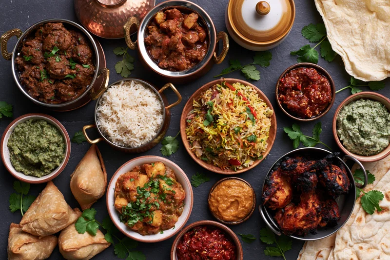 Overhead spread of indian dishes arranged on dark slate surface