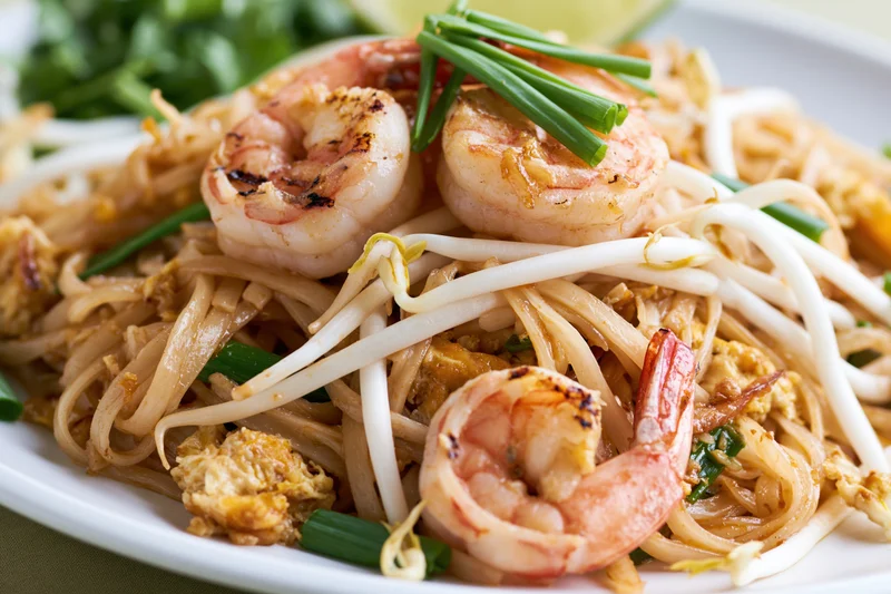 Pad thai noodles with grilled shrimp and scrambled egg served on a white plate garnished with bean sprouts and green onions