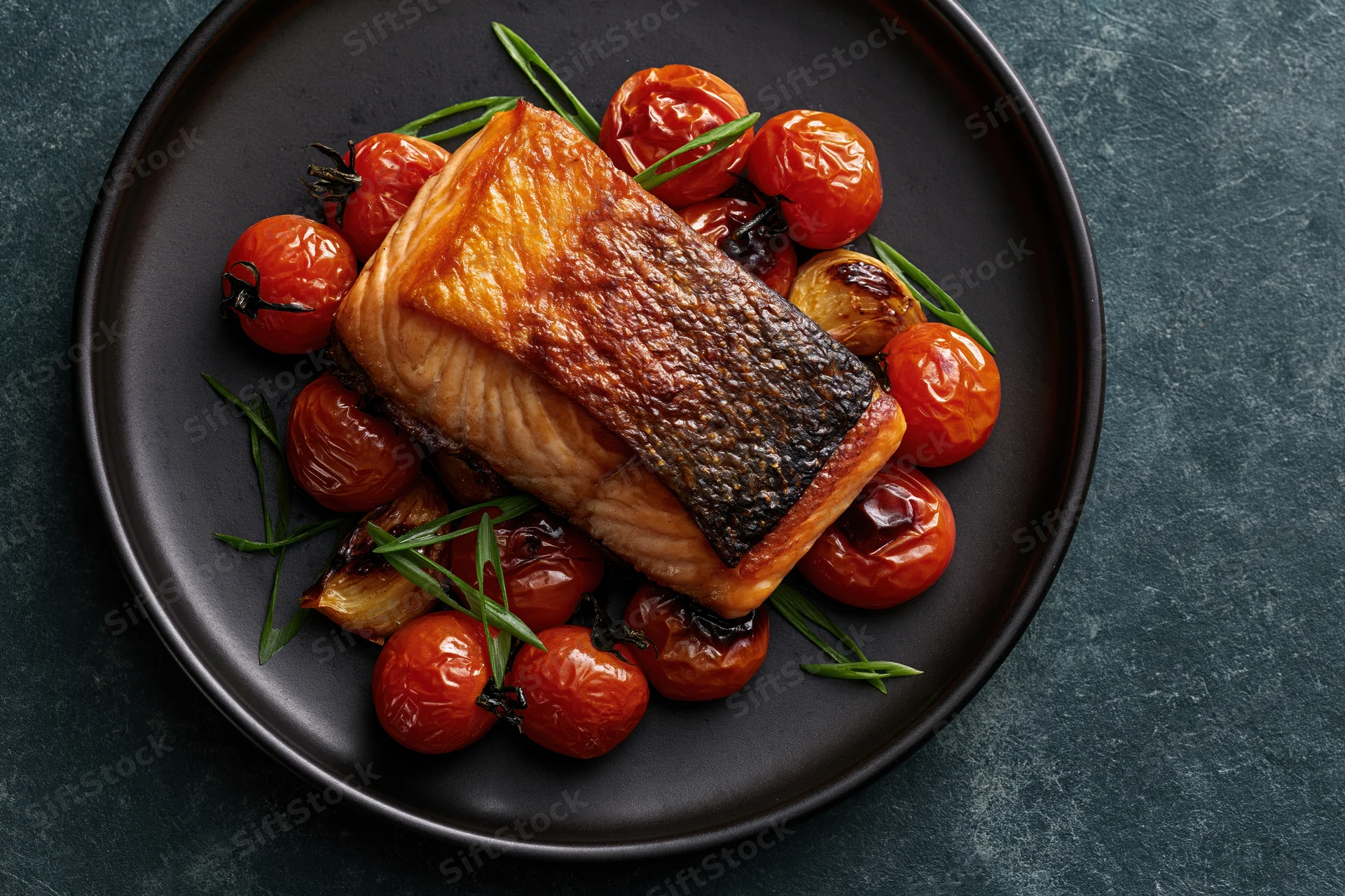 Pan-seared salmon fillet with roasted tomatoes and herbs on a dark matte ceramic plate